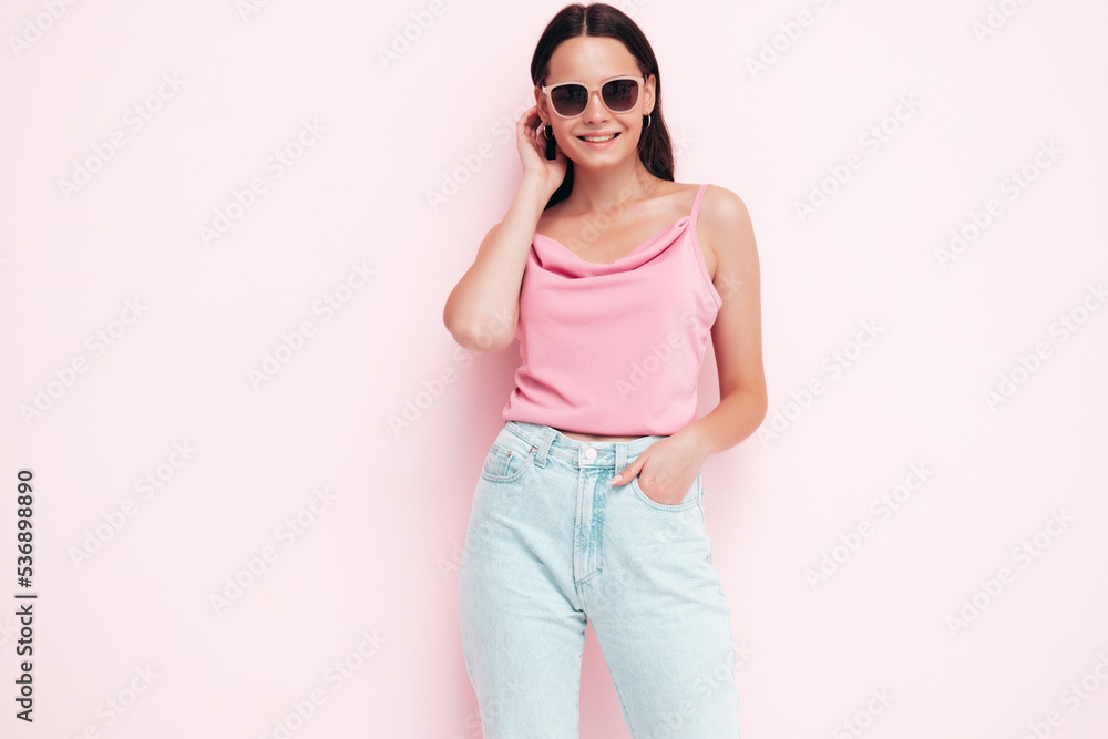 Young beautiful smiling female in trendy summer clothes. carefree woman posing near pink wall in studio. Positive brunette model having fun and going crazy. Cheerful and happy. In sunglasses Young beautiful smiling female in trendy summer clothes. carefree woman posing near pink wall in studio. Positive brunette model having fun and going crazy. Cheerful and happy. In sunglasses