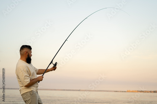 Fishing at sunset. Young man fishing on lake with sky background