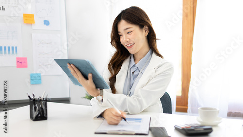 Businesswoman using laptop to work, Asian woman working in the office, Financial clerk or accountant with documents and equipment working on the desk, Using tablet for financial transactions. © Puwasit Inyavileart