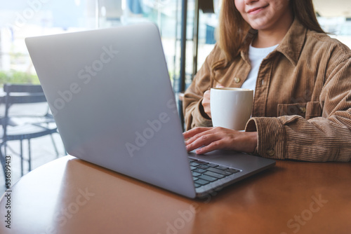 Closeup image of a woman using and working on laptop computer while drinking coffee