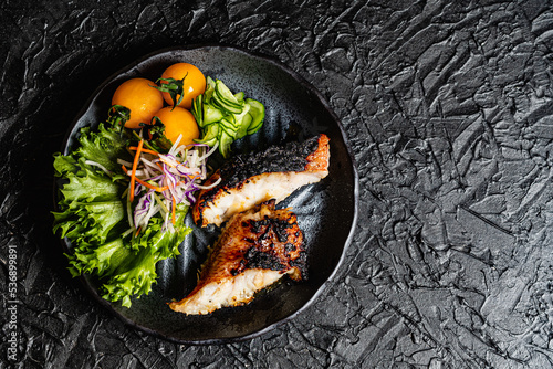 Grilled tilefish marinated with saikyo-miso and tomato salad on a black plate against a black design board. photo