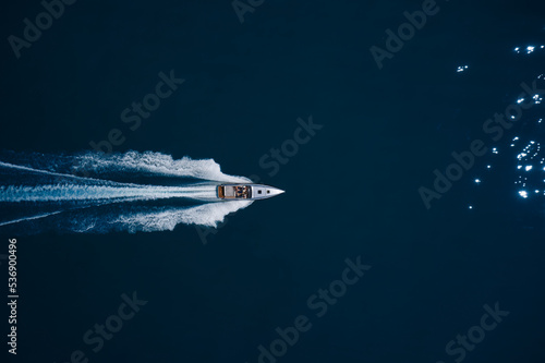 super fast open big boat with people moving fast on dark blue water making a white trail behind the boat. © Berg