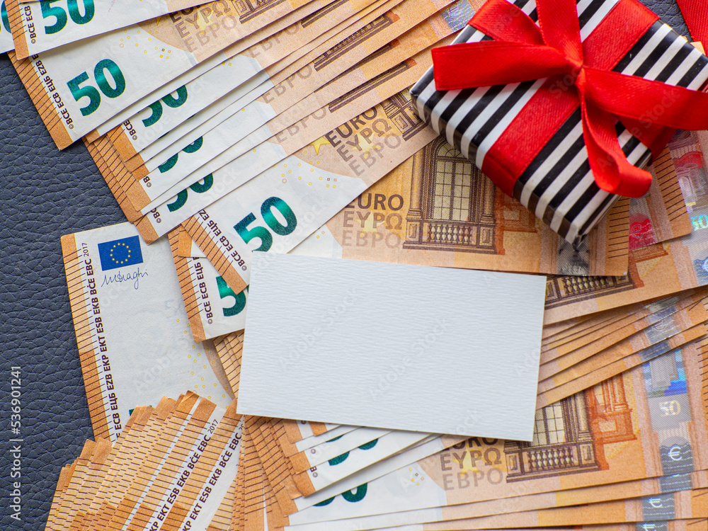 Fototapeta premium Blank sheet with copy space on the background of fifty euros banknotes with gift box. Set of European Union money. Enterprise capital investment, finance, savings, buying gifts, spending money concept
