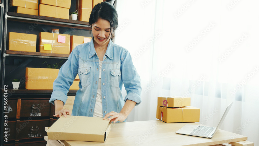 Woman packing box on table checking goods package delivery shipping to customer. Asian woman startup small business at home office desk. Entrepreneur asian woman packing product for delivery items Woman packing box on table checking goods package delivery shipping to customer. Asian woman startup small business at home office desk. Entrepreneur asian woman packing product for delivery items