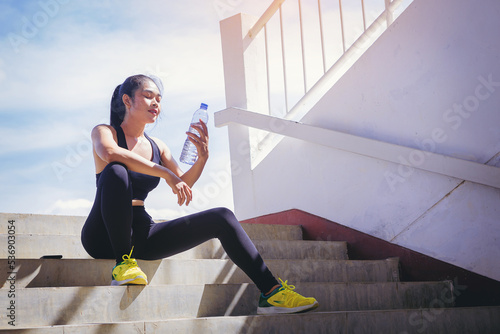 Tired runner woman with a bottle of electrolyte drink freshness after training outdoor workout at the stadium stairway.