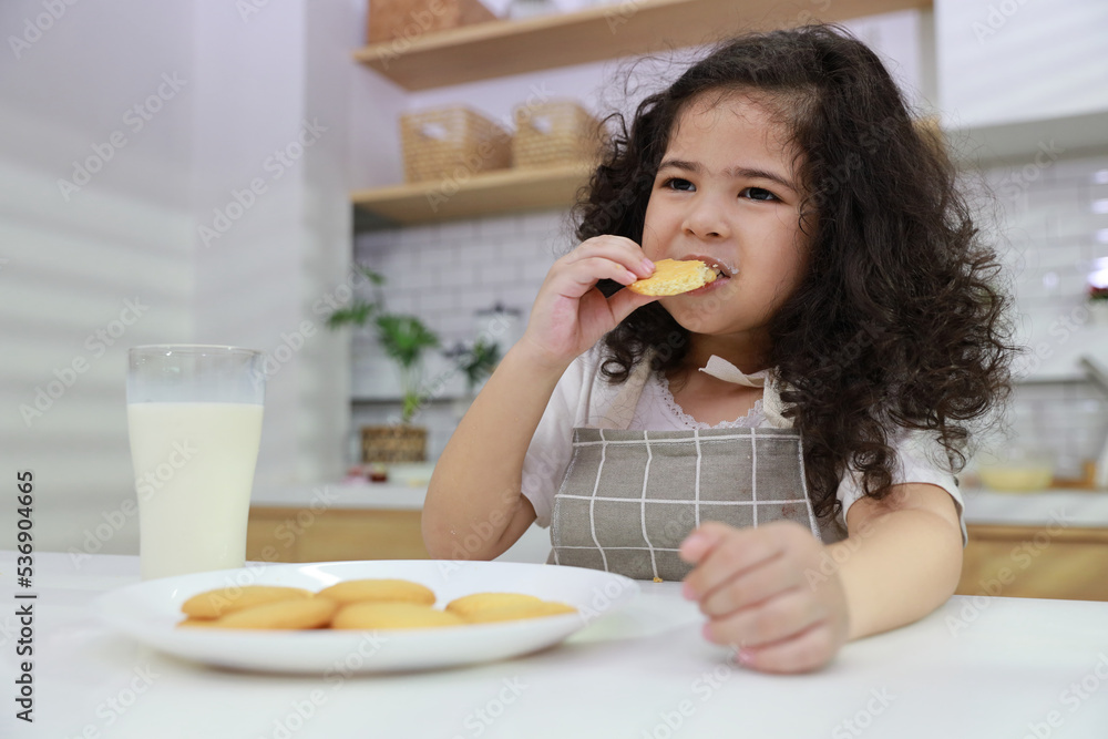 Young hispanic currly hair girl sitting on table and drinking milk while eating vanilla cookies for breakfast with enjoying time. Tasty food and delicious food with happy meal lifestyle kid concept Young hispanic currly hair girl sitting on table and drinking milk while eating vanilla cookies for breakfast with enjoying time. Tasty food and delicious food with happy meal lifestyle kid concept