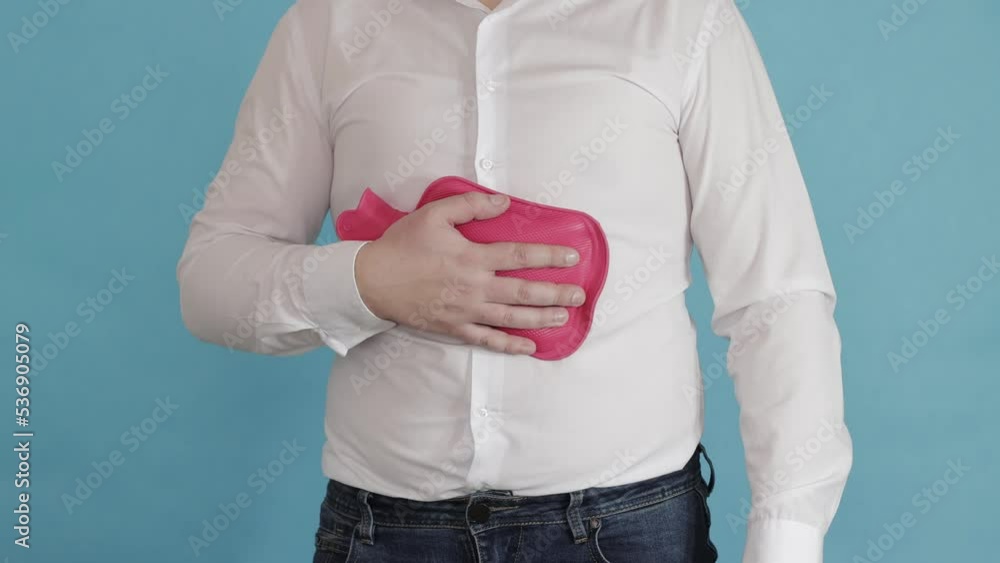 A man in a white shirt puts a red heating pad on his stomach. The