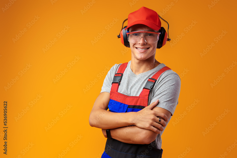 Young construction worker in helmet and uniform posing on yellow background in studio Young construction worker in helmet and uniform posing on yellow background in studio