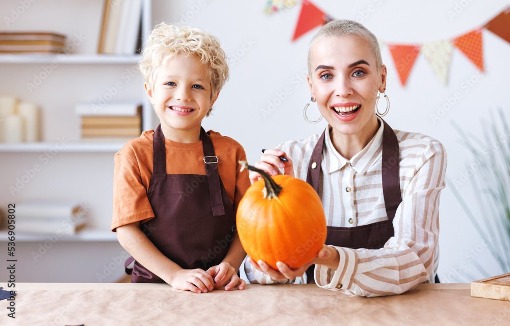 Fototapeta premium Son and mom making Jack-o-Lantern together at home, painting Halloween pumpkin