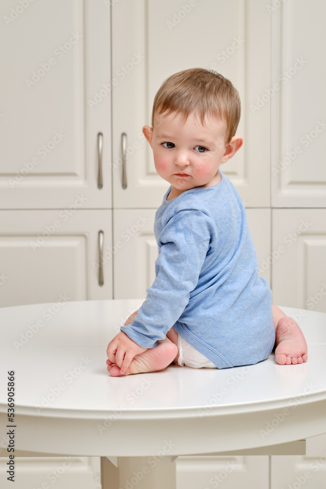 Toddler baby climbed on the kitchen white table. A child in danger climbed to the top, risking falling off the furniture. Kid aged one year and two months Toddler baby climbed on the kitchen white table. A child in danger climbed to the top, risking falling off the furniture. Kid aged one year and two months