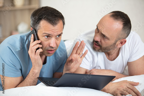 gay couple looking at laptop and having phone call