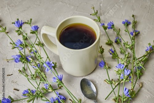 chicory drink in a coffee mug and a spoon next to chicory flowers