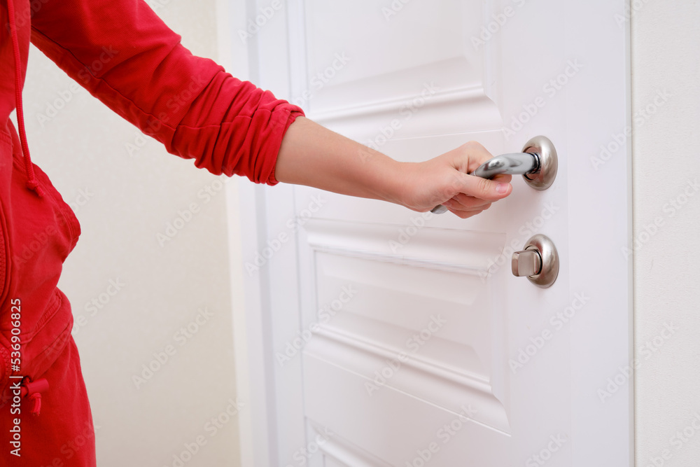 A woman opens the door holding the handle, hand close-up. White wooden door, metal door handle and female hand - obrazy, fototapety, plakaty 