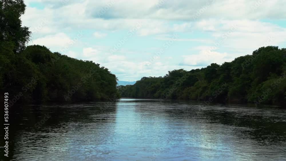 4K shot from the middle of a large Brazilian river with a gentle current surrounded by jungle foliage in the state of Bahia, northeastern Brazil on a warm overcast summer day. 4K shot from the middle of a large Brazilian river with a gentle current surrounded by jungle foliage in the state of Bahia, northeastern Brazil on a warm overcast summer day.