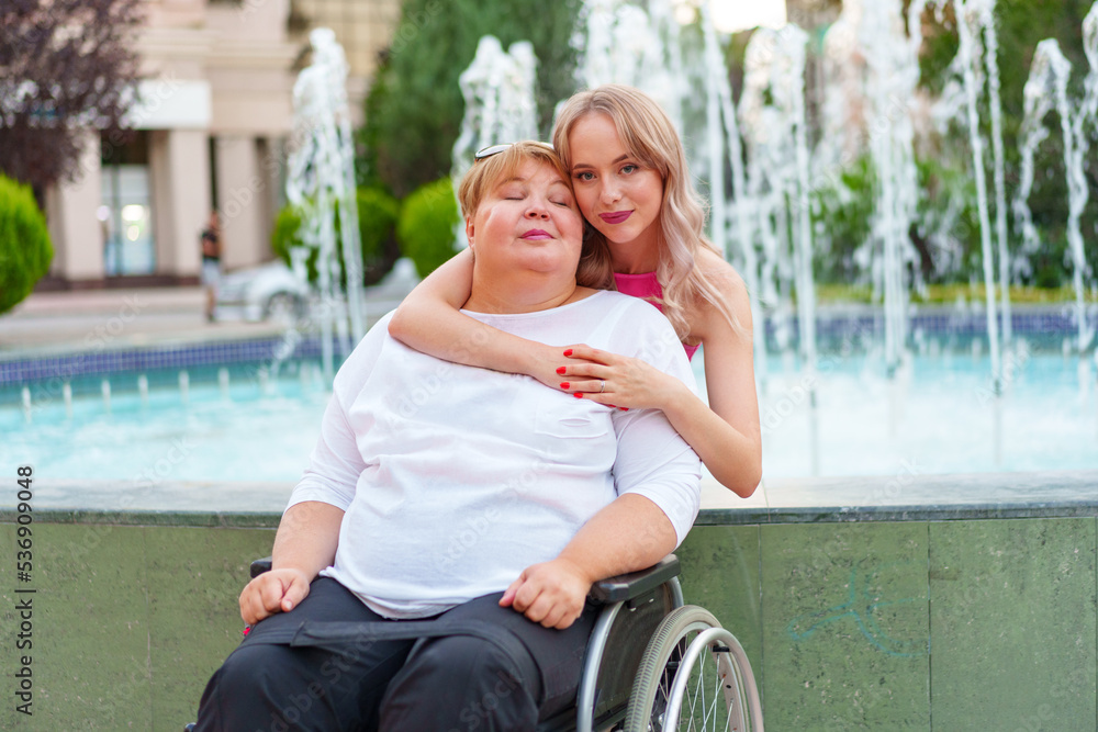 Young daughter taking care of her mother with disability sitting in wheelchair Young daughter taking care of her mother with disability sitting in wheelchair