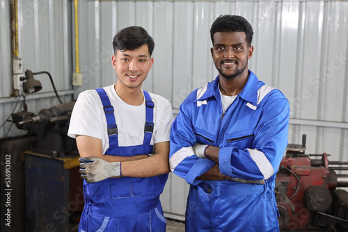 Multiethnic technicain mechanic crossed arms with confident while working on metal lathe machine operate polishing car disc brake at garage. Maintenance automotive and inspecting vehicle part concept photo