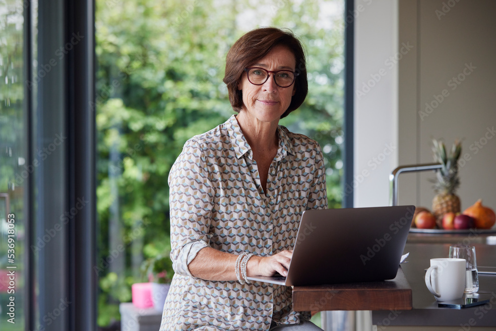 Senior woman with laptop sitting at kitchen island Senior woman with laptop sitting at kitchen island