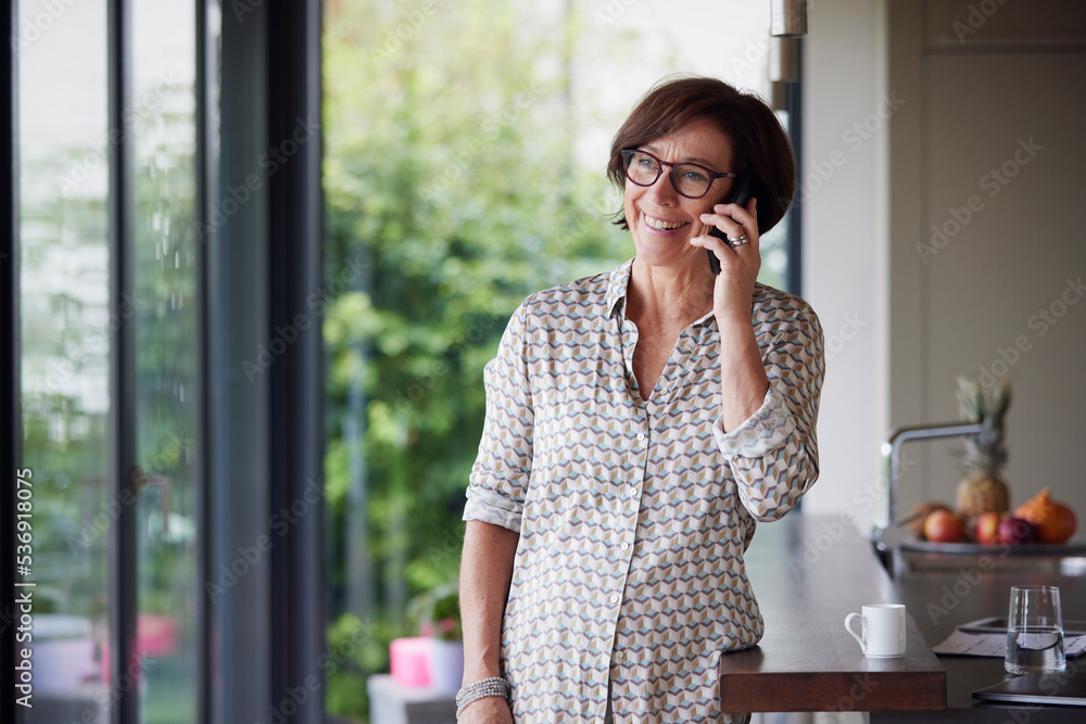 Happy senior woman talking on smart phone standing by kitchen island at home Happy senior woman talking on smart phone standing by kitchen island at home