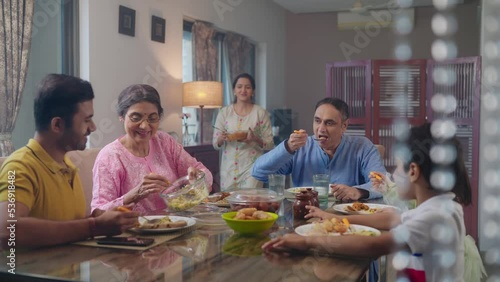 An entire happy Indian South Asian ethnic loving family members including parents, grandparents, and kids or children are having lunch, or a meal together in an indoor home. Relationship, food concept