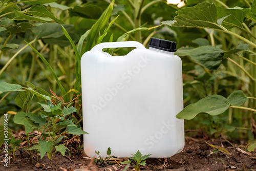 Blank mockup white plastic jug for herbicide chemical in cultivated sunflower field