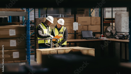 Two warehouse employees reading a clipboard while moving goods with a pallet truck in a logistics center photo