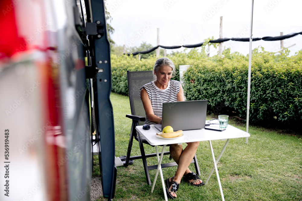 Freelancer using laptop sitting outside camper van Freelancer using laptop sitting outside camper van