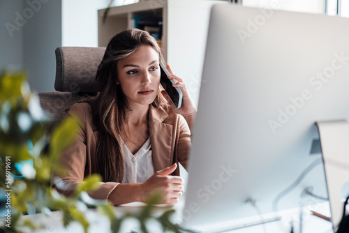 Young businesswoman talking on mobile phone in front of desktop PC photo