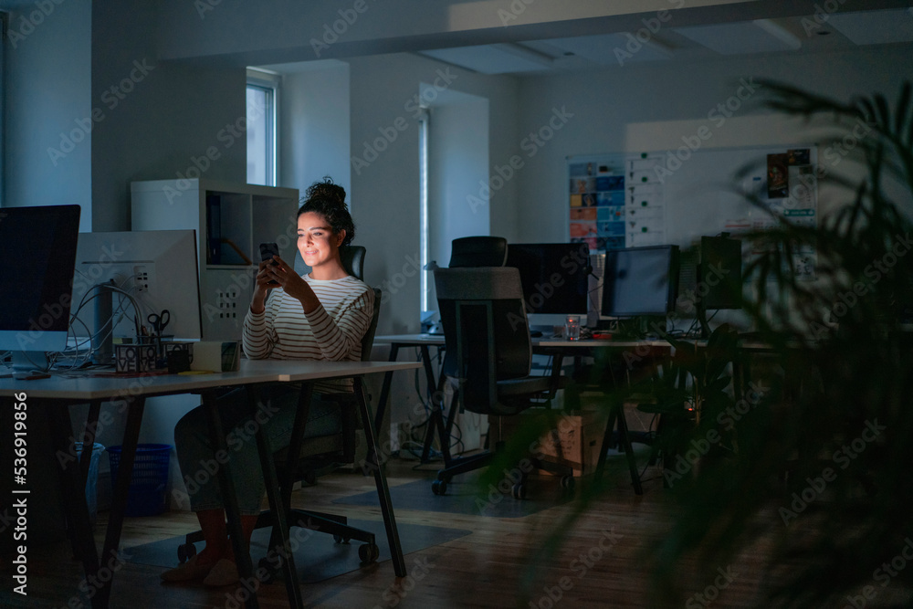 Smiling woman using smart phone in dark office Smiling woman using smart phone in dark office
