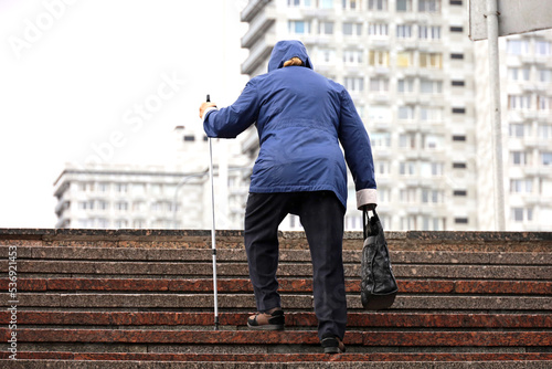 Old woman with walking cane climbing stairs on city street. Concept for disability, limping adult, diseases of the spine © Oleg