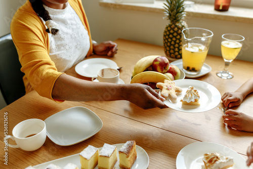 Hand of woman holding plate of lemon meringue pie and gingerbread at dining table photo