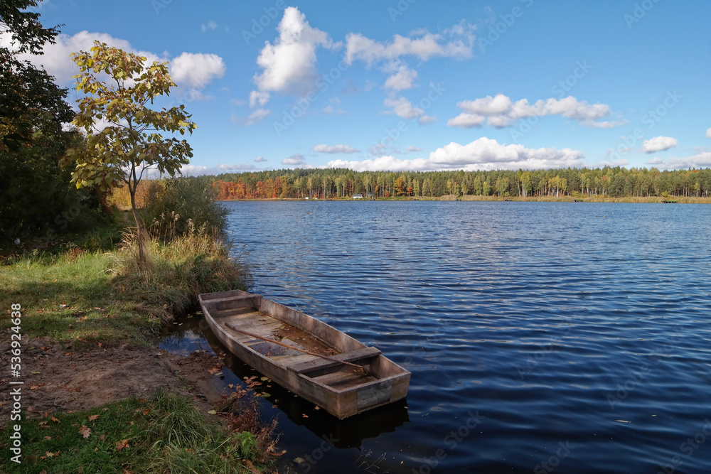 Widok na jezioro i łódkę w jesiennej odsłonie.
