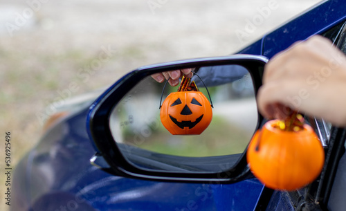 smiling plastic halloween pumpkin mini small pumpkin in reflection rear view retractable lateral mirror.woman hand holding pumpkin bucket handle.trick or treat holiday, car auto vehicle vehicle part