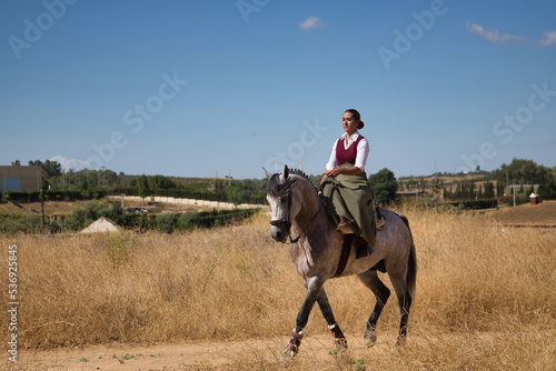 Woman horsewoman, young and beautiful, walking, riding her horse, in the countryside. Concept horse riding, animals, dressage, horsewoman, cowgirl.