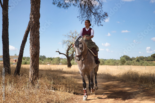 Woman horsewoman  young and beautiful  running at a trot with her horse  on a path with pine trees in the countryside. Concept horse riding  animals  dressage  horsewoman  cowgirl.