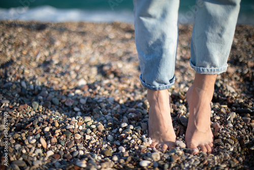 Fototapeta Naklejka Na Ścianę i Meble -  Barefoot massage grounding healthy step on a stone beach seaside. Relaxing vacation photo women legs in jeans banner selective focus macro narrow grip.