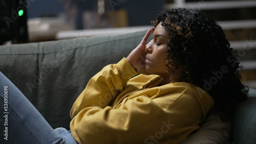 One upset young black woman feeling frustration. An anxious African American girl laid on sofa in living room at night