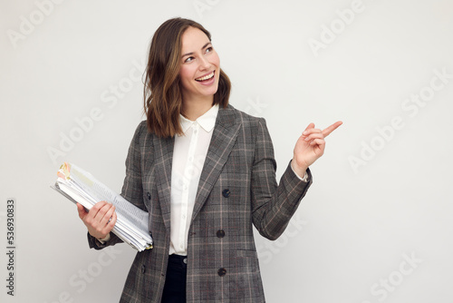 Beautiful and smiling business woman with paperwork in hands, standing isolated on white, looking happy about work pointing on copy space. Your logo or text on white background. 