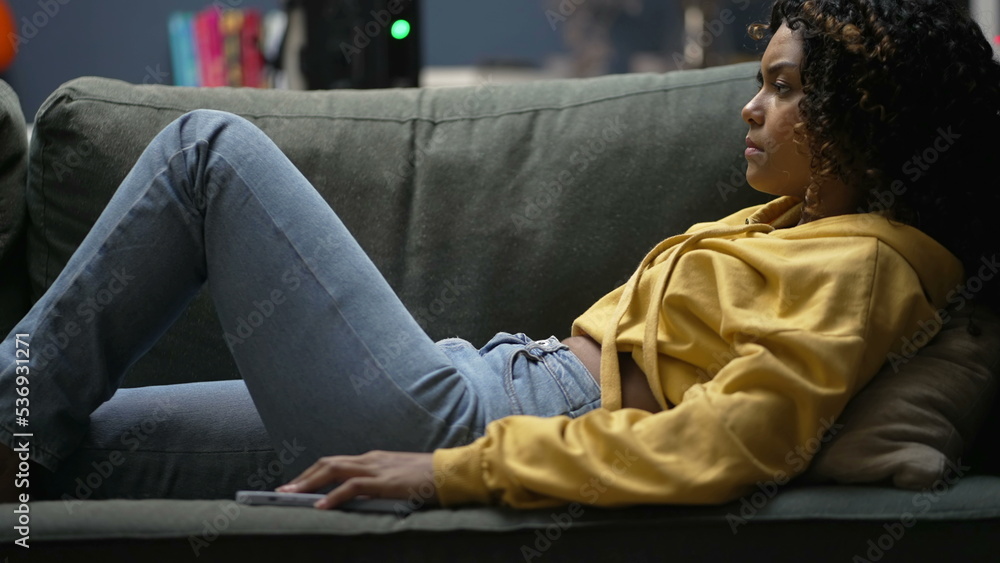 One angry black girl upset to cellphone message. Young woman not liking notification on smartphone device laid on couch sofa One angry black girl upset to cellphone message. Young woman not liking notification on smartphone device laid on couch sofa