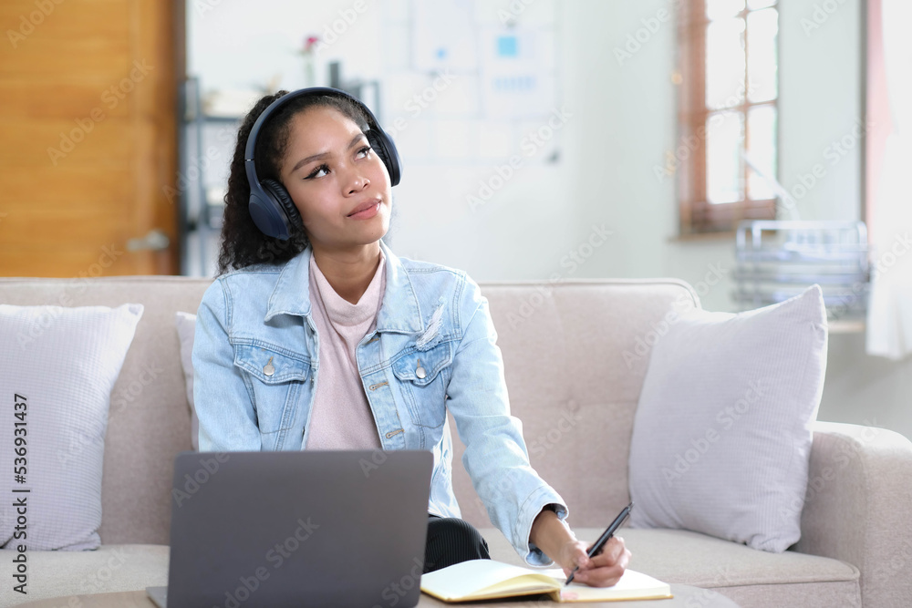 Smiling Asian young female using headphones looking at laptop screen listen and learning online courses. Smiling Asian young female using headphones looking at laptop screen listen and learning online courses.