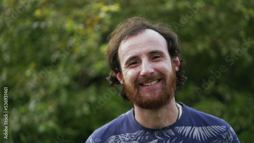 Joyful closeup face of a red hair casual man with beard smiling at camera. Headshot of redhead portrait standing outdoors with happy emotion