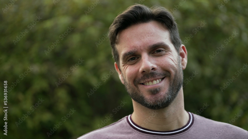 Happy handsome man standing at park smiling at camera. 30s closeup portrait male face closeup with beard Happy handsome man standing at park smiling at camera. 30s closeup portrait male face closeup with beard