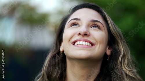 Happy hopeful young millennial woman standing outside smiling looking at sky with FAITH