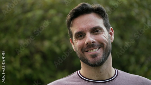 Happy handsome man standing at park smiling at camera. 30s closeup portrait male face closeup with beard