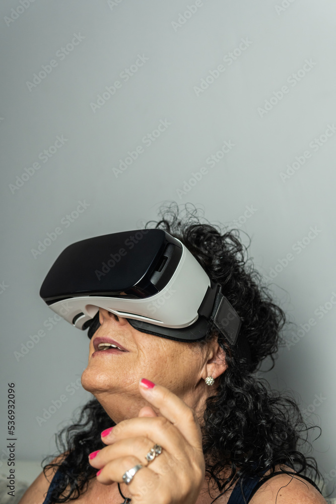 Vertical shot of older curly-haired brunette woman experiencing 3D generated space with virtual reality goggles. Vertical shot of older curly-haired brunette woman experiencing 3D generated space with virtual reality goggles.