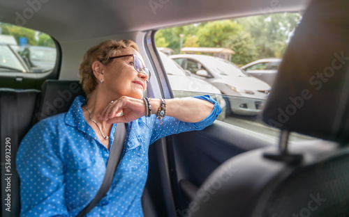Beautiful happy senior woman in a blue blouse in the passenger seat in a car enjoying a trip