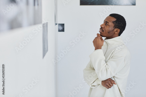 Side view portrait of handsome black man looking at images in photo gallery and enjoying art, copy space