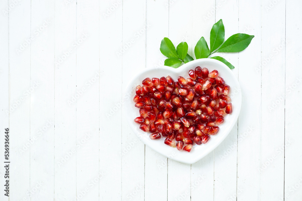 Top view pomegranate seed on white plate with green leaves on white wood background. Top view pomegranate seed on white plate with green leaves on white wood background.