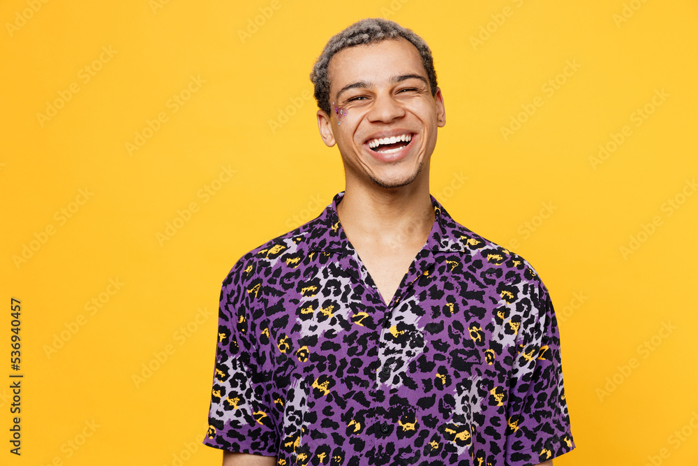 Young laughing smiling happy fun cheerful cool gay man wearing purple animal print shirt looking camera isolated on bright plain yellow color background studio portrait. Lifestyle lgbtq pride concept. Young laughing smiling happy fun cheerful cool gay man wearing purple animal print shirt looking camera isolated on bright plain yellow color background studio portrait. Lifestyle lgbtq pride concept.