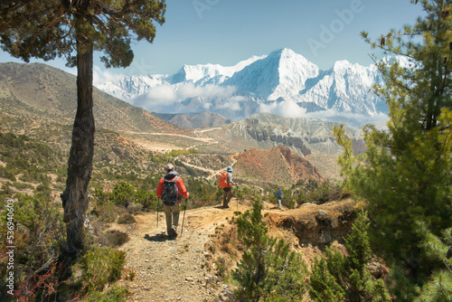 Group of tourists with backpacks descends down mountain trail during hike in Upper Mustang, Nepal.