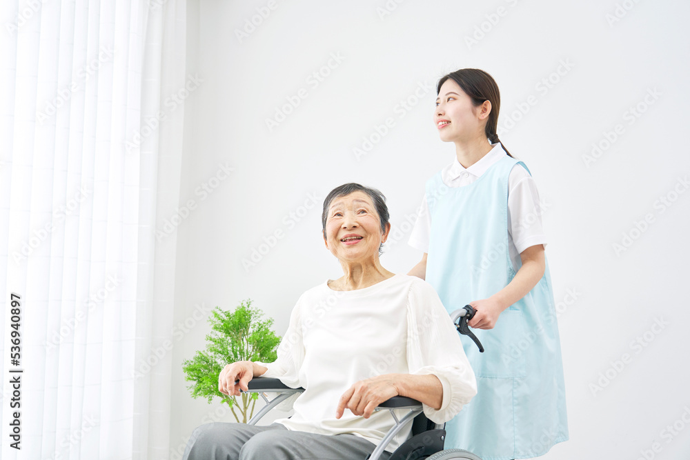 室内で高齢者女性の乗った車椅子を押す介護士